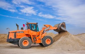 An orange construction machine equipped with a sturdy scoop, effortlessly moving a large pile of earth at a construction site with hydraulics