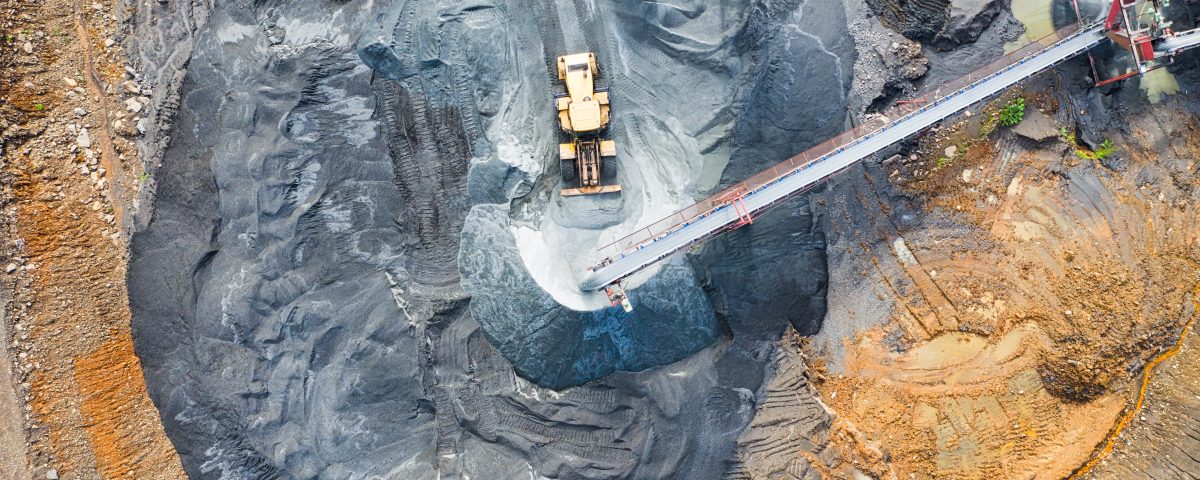 Aerial view of a sprawling mine site, showing the intricate network of roads, equipment, and mining operations. Massive machinery, including trucks and excavators, can be seen moving across the rugged terrain. The mine is a hive of activity, highlighting the scale and complexity of the mining industry.