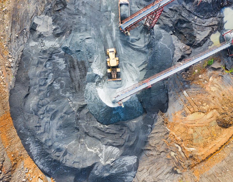 Aerial view of a sprawling mine site, showing the intricate network of roads, equipment, and mining operations. Massive machinery, including trucks and excavators, can be seen moving across the rugged terrain. The mine is a hive of activity, highlighting the scale and complexity of the mining industry.